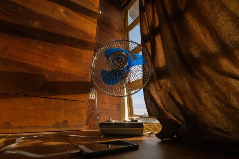 A nostalgic scene featuring an electric fan and cellphone by a sunlit curtain.